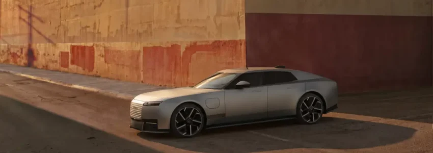 Silver Jaguar Type 01 electric grand tourer beside an industrial wall.